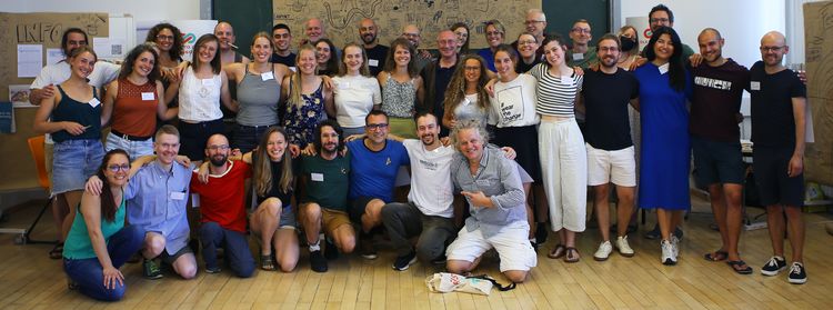 Gruppe von Menschen in einem Seminarraum vor einer beschriebenen Tafel und Flipcharts