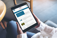 Tablet haltende, sitzende Person, auf dem NHS-Newsletter erscheint