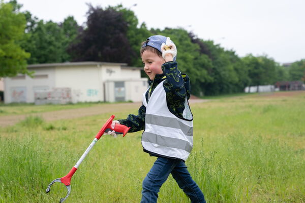 Sauberhafter Kindertag, Kind sammelt Müll auf einer Wiese ein